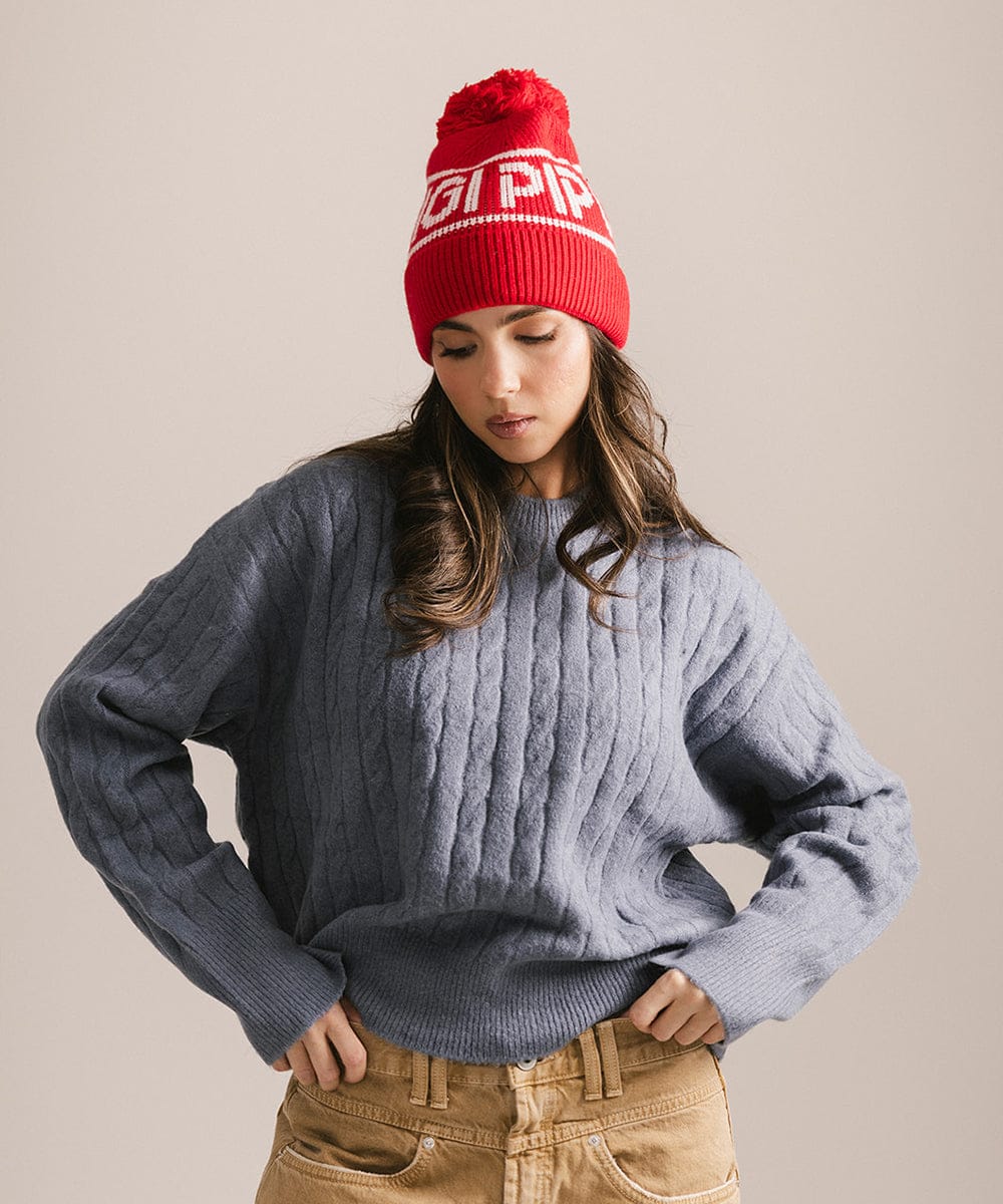 Woman wearing a red beanie with text and a gray sweater on a beige background #color_ruby red