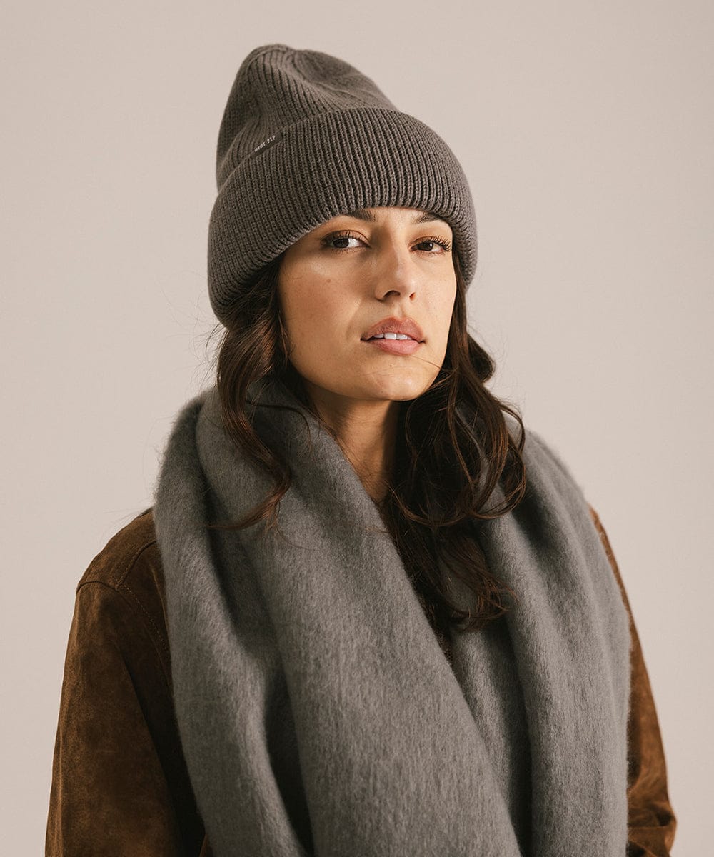 Woman wearing a gray knit beanie and scarf against a beige background #color_grey