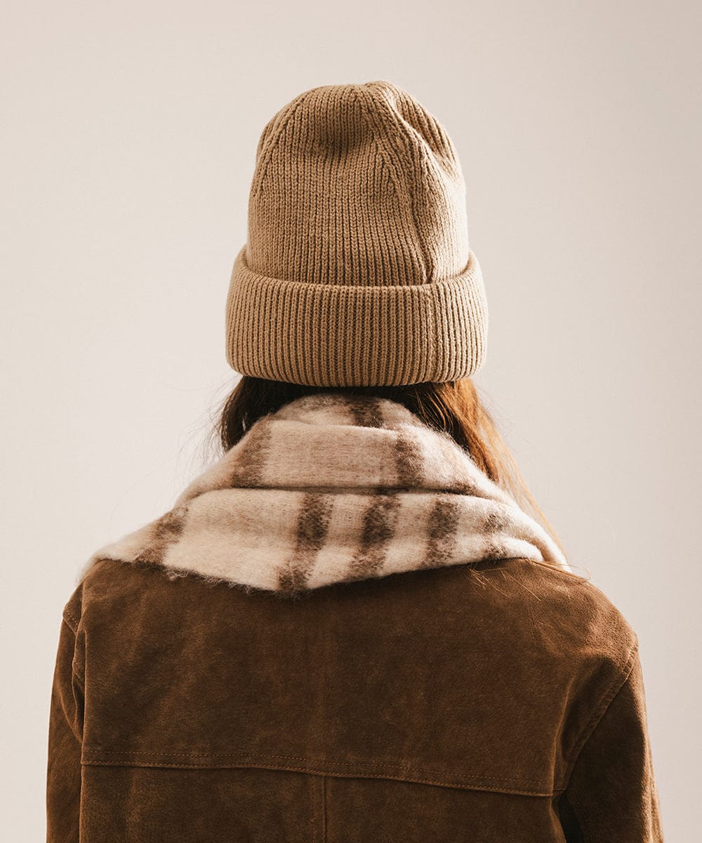 Person wearing a brown knit beanie and coat with fur collar on a plain background #color_tan
