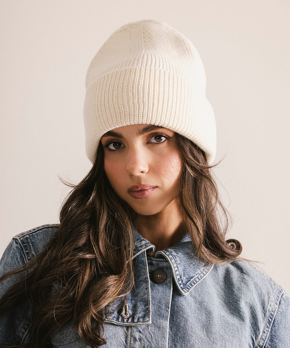 Woman wearing a beige knit beanie and denim jacket against a plain background #color_off white