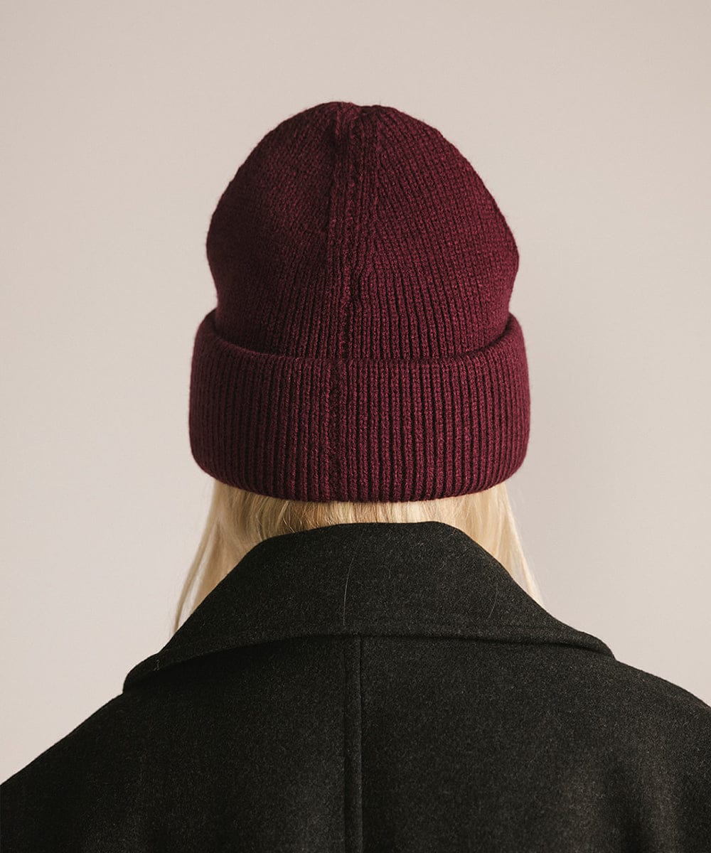 Person wearing a maroon beanie and dark coat on a beige background #color_merlot