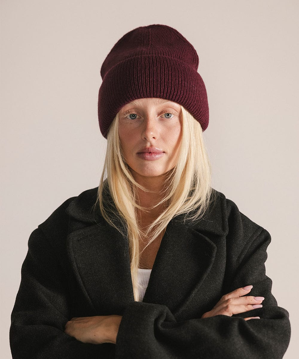 Person wearing a maroon beanie and black coat against a plain background #color_merlot