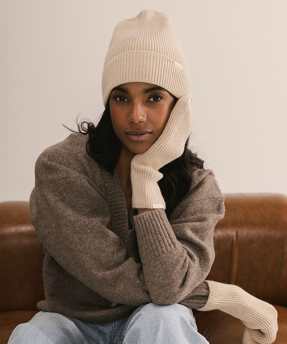 Woman wearing a beige knit hat and sweater sitting on a brown couch. #color_taupe