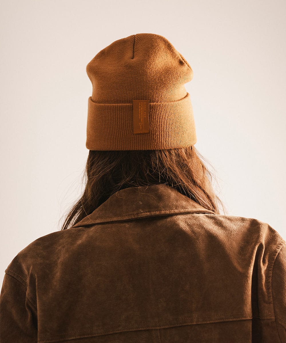 Person wearing a brown beanie and coat against a plain background #color_cocoa