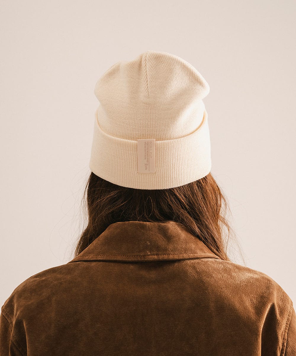 Person wearing a beige beanie and brown coat against a plain background #color_cream