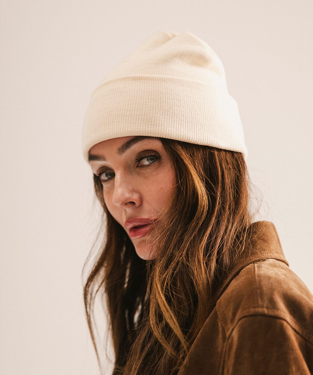 Woman wearing a white beanie and brown jacket against a plain background #color_cream