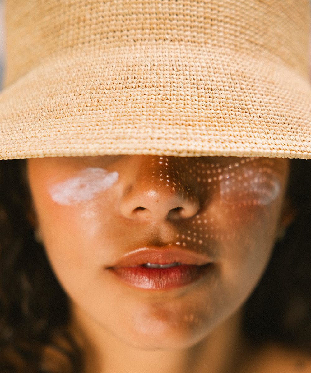 Close-up of a woman wearing a straw hat with sunscreen on their face #color_natural