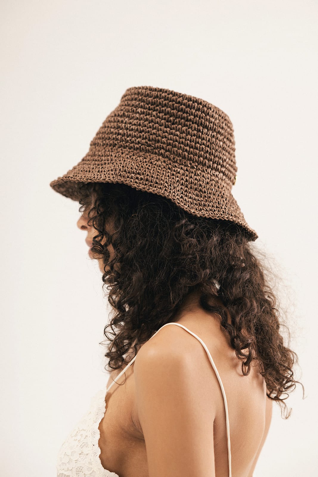 Woman wearing a brown woven bucket hat against a plain background #color_chocolate