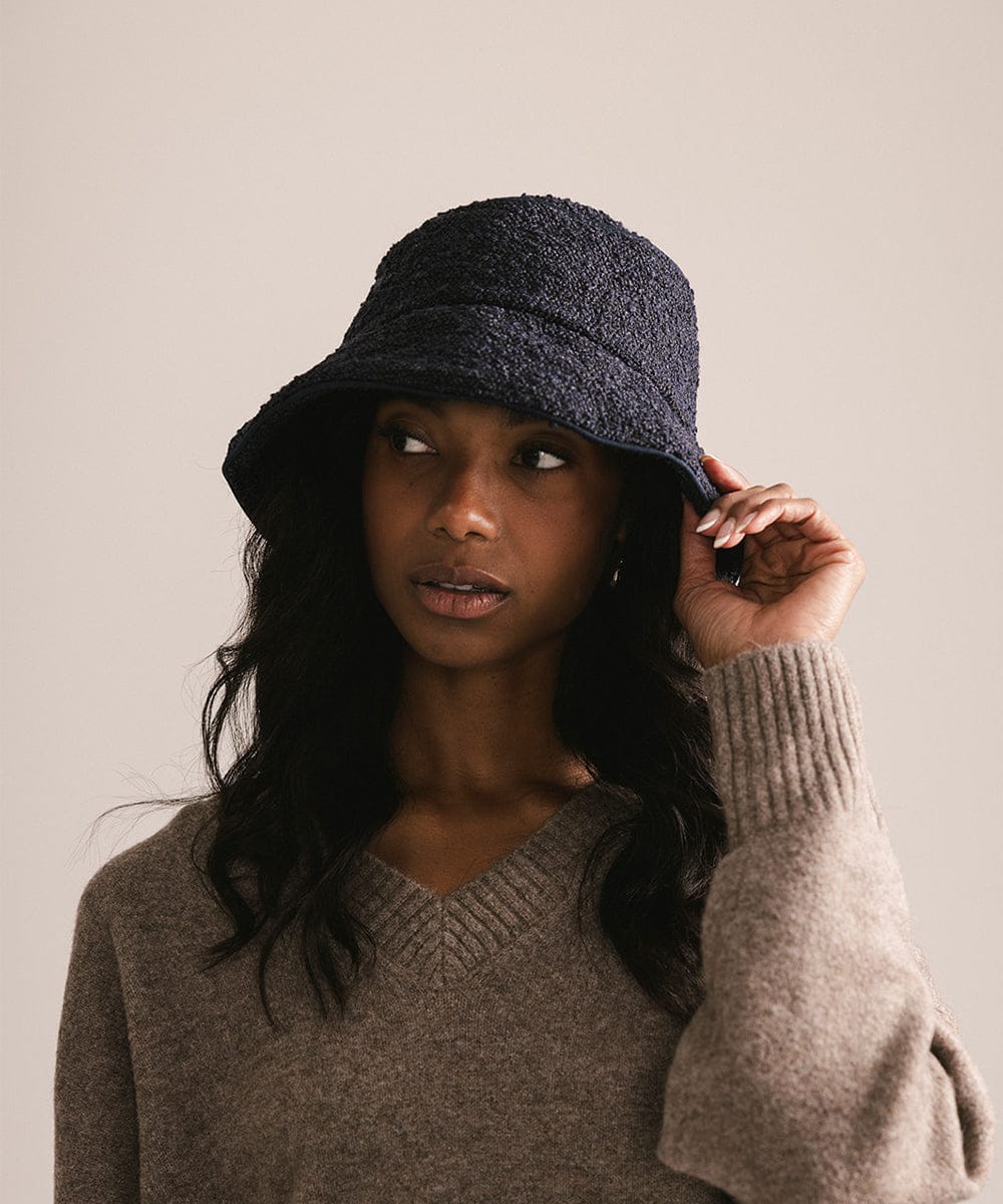 Woman wearing a dark blue bucket hat and brown sweater against a plain background #color_navy