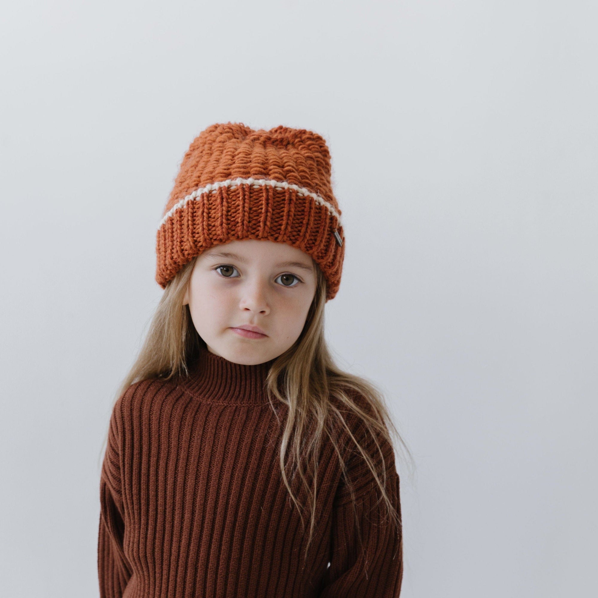Gigi Pip beanies for kids - Kids Vail Beanie - 100% acrylic chunky knit beanie in a universal kids size featuring a comfortable plush inner band and the Gigi Pip logo on a metal bar in the front [cream + burnt orange]