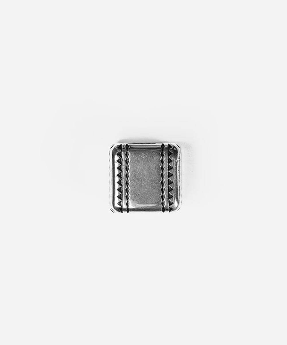 A small rectangular silver-toned metal charm or pendant with decorative triangular cutouts along the borders, centered on a plain light gray background #color_silver