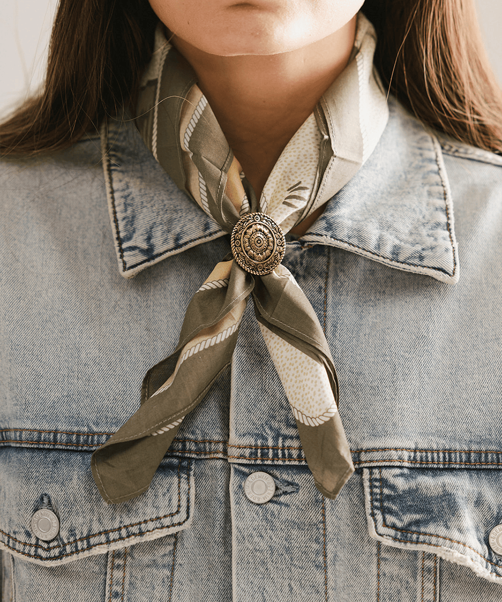 Person wearing a denim jacket with a green scarf tied around the neck, featuring a Floral Oval Concho Bandana Slide. #color_gold