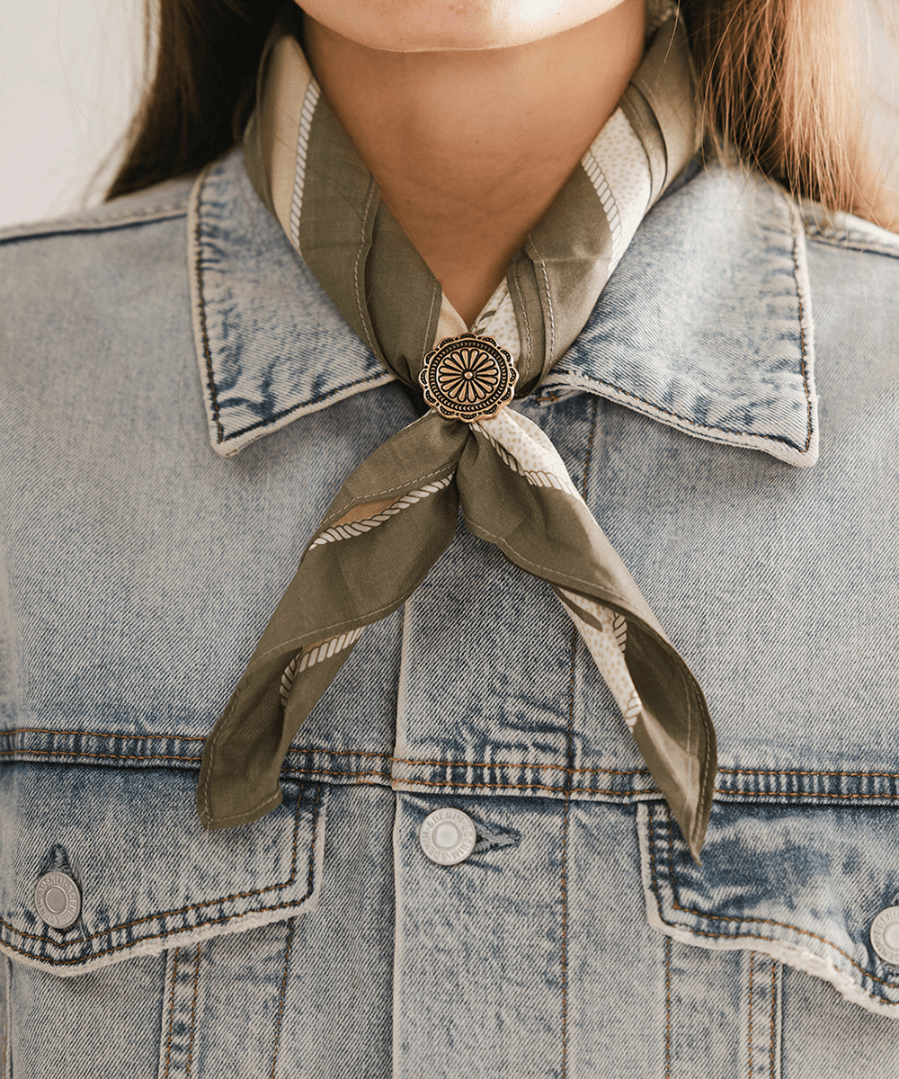 Person wearing a denim jacket with a green scarf tied with a Sunburst Concho Bandana Slide around the neck #color_gold