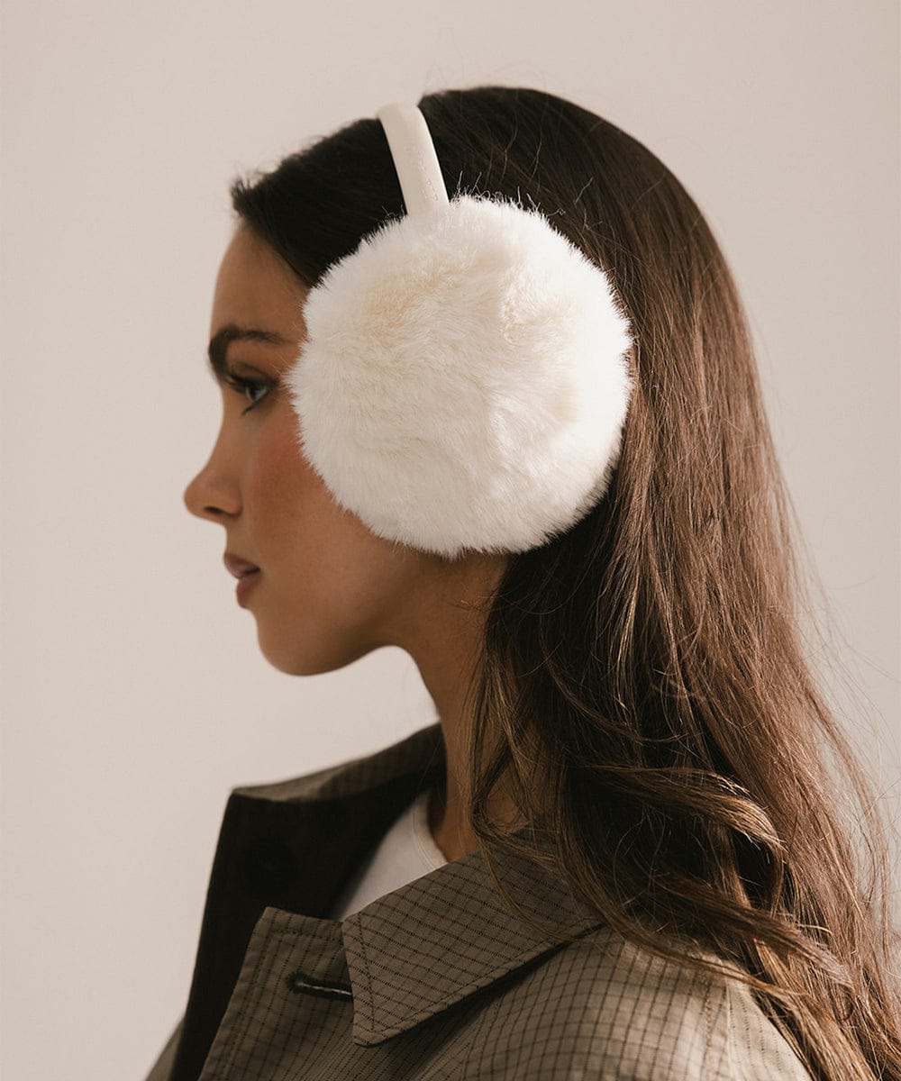 Woman wearing white fluffy earmuffs against a neutral background #color_winter white