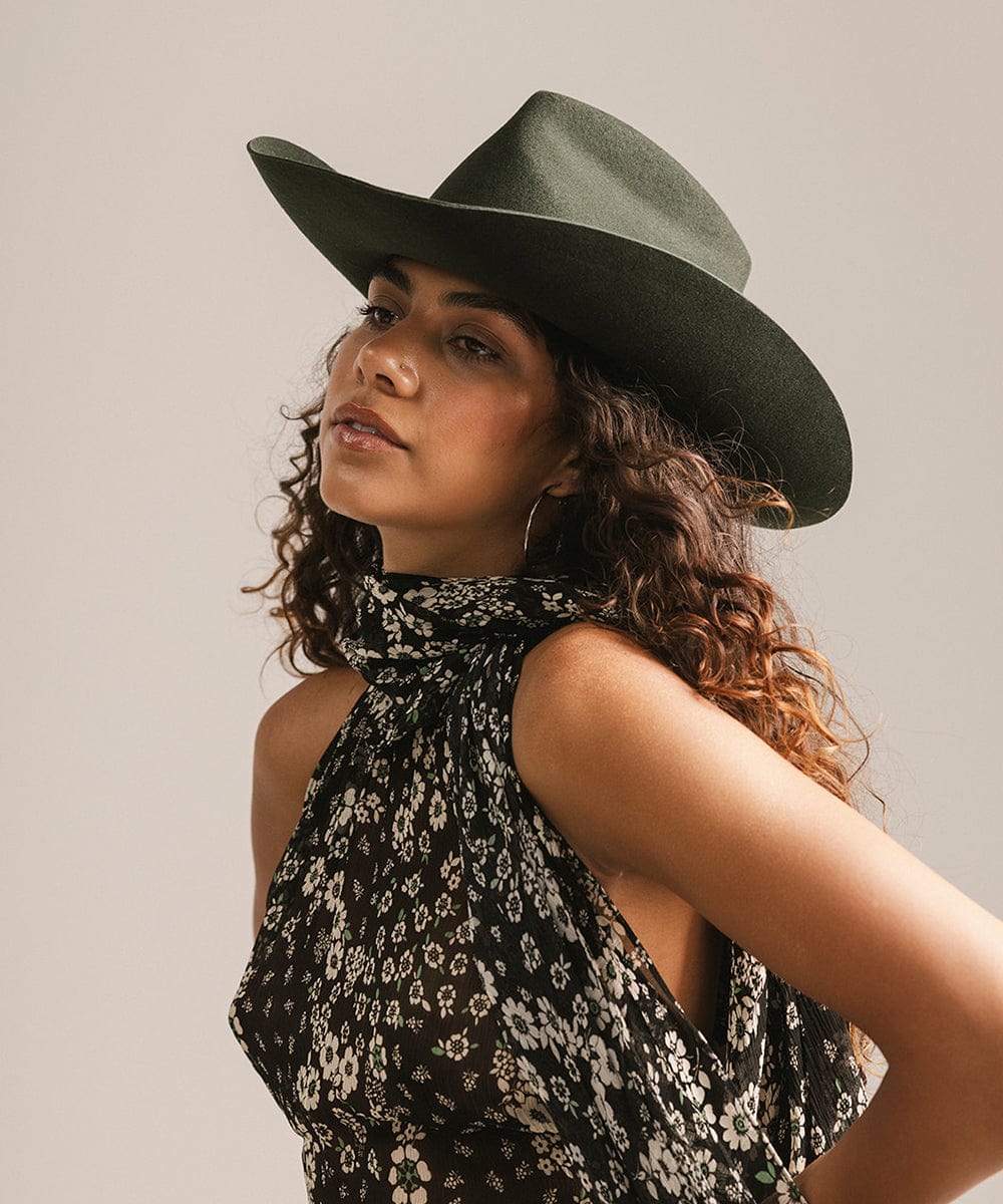 Woman wearing a green cowboy hat and a black floral dress against a plain background #color_dark green