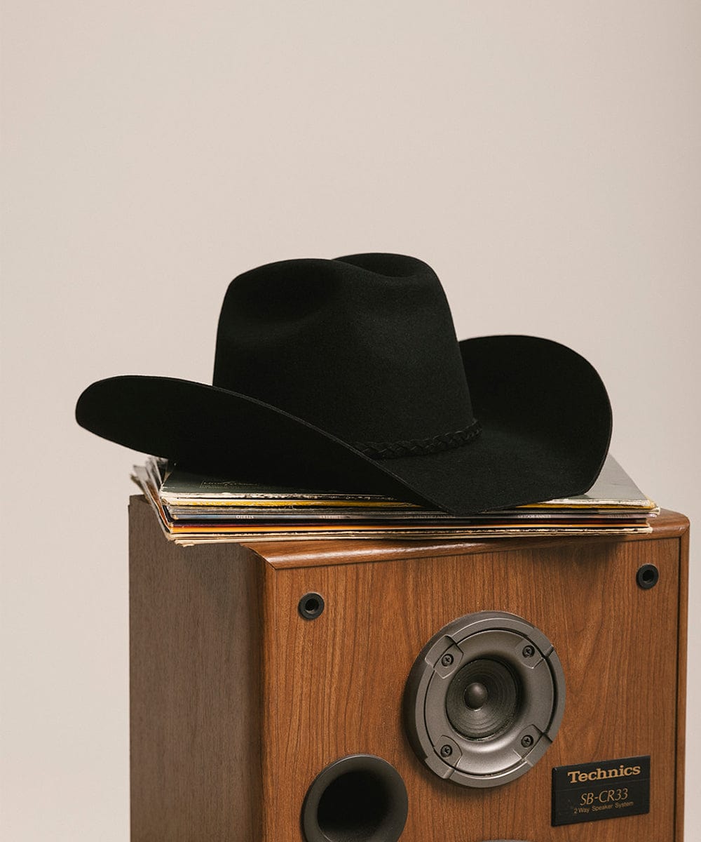 Black cowboy hat on a Technics record player with vinyl records against a beige background #color_black