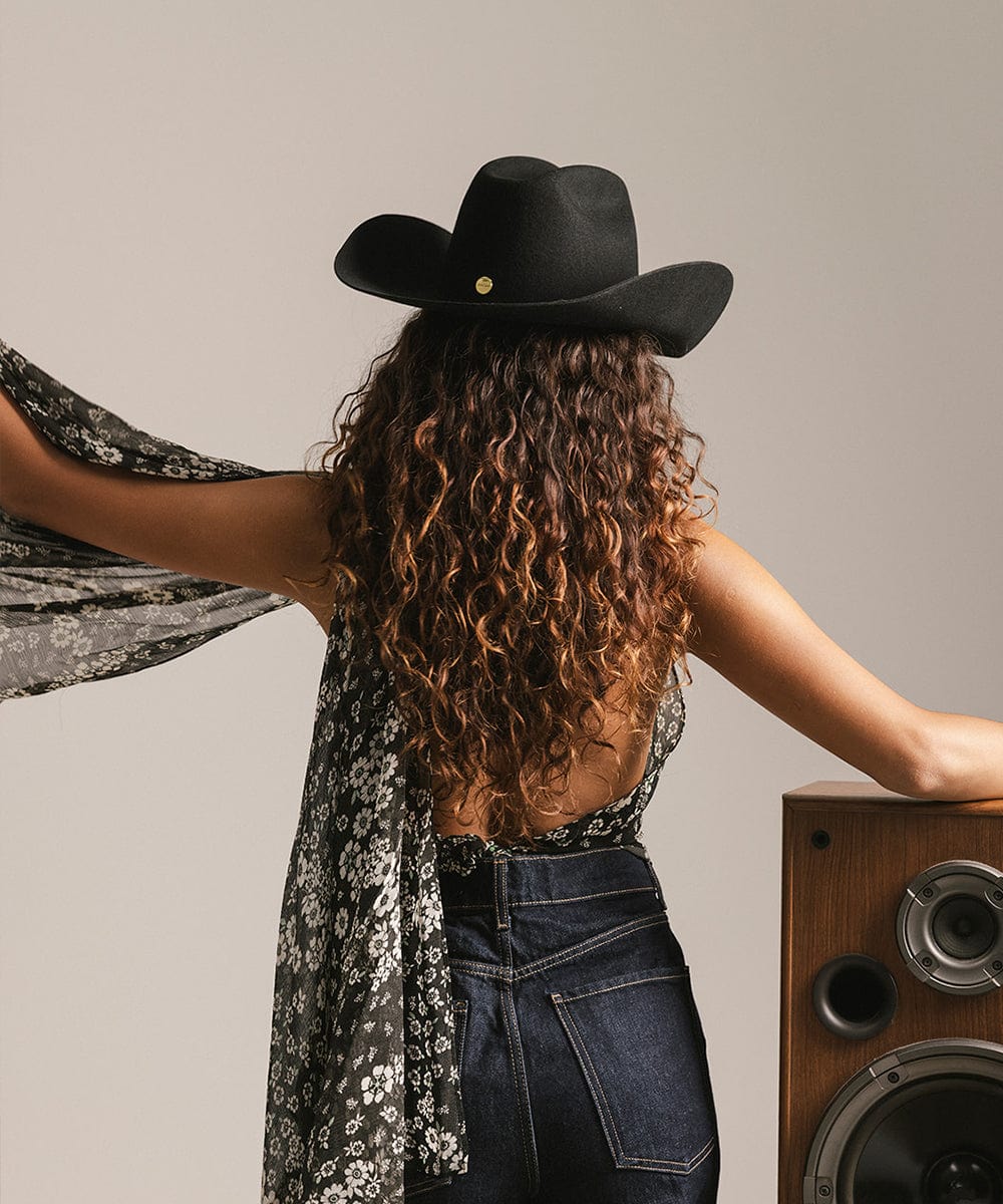 Person wearing a black cowboy hat and floral scarf, standing next to a wooden speaker. #color_black