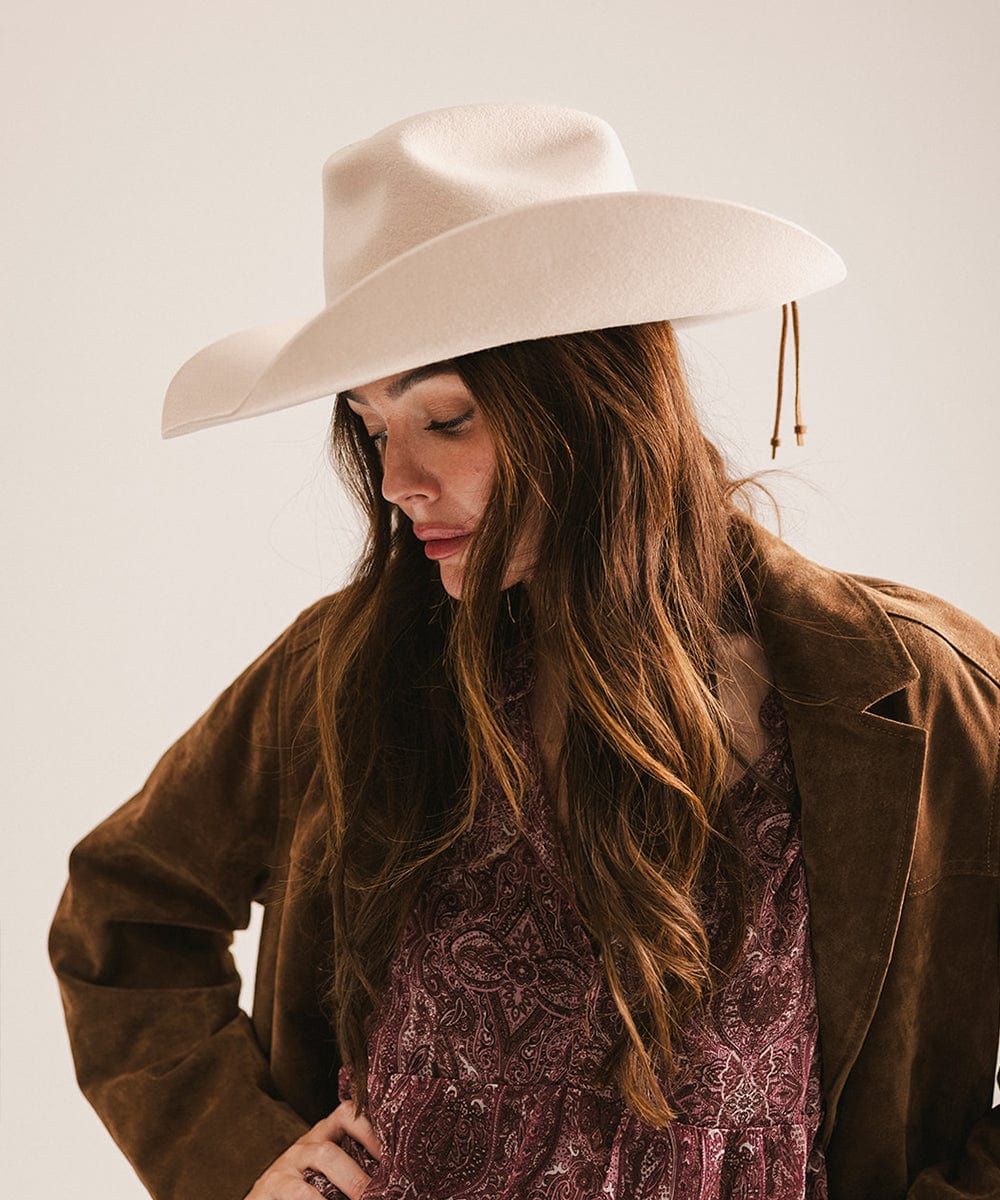 Woman wearing a beige cowboy hat and brown jacket against a plain background #color_cream