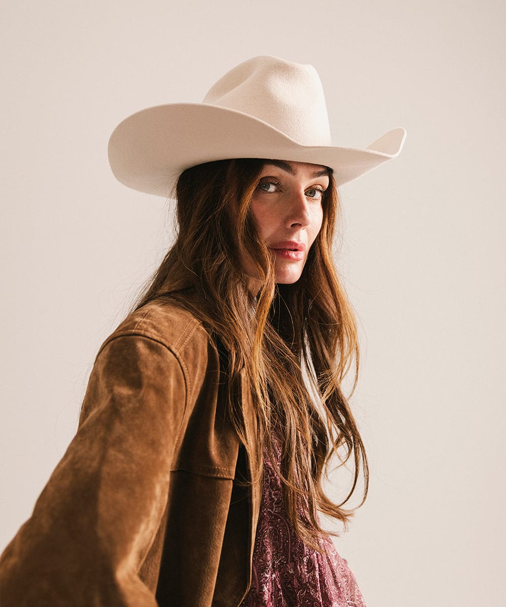 Woman wearing a white cowboy hat and brown jacket against a plain background #color_cream