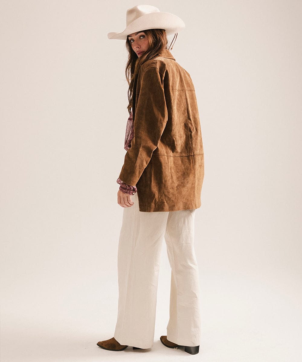 Person wearing a brown jacket, white pants, and a white hat on a plain background #color_cream