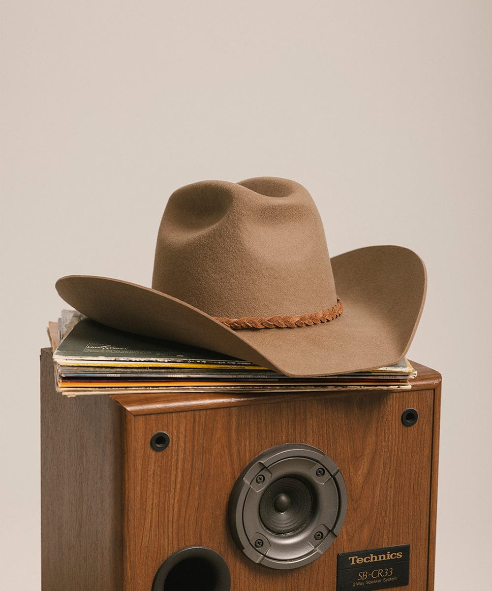 Brown cowboy hat on a Technics record player with vinyl records against a beige background #color_brown