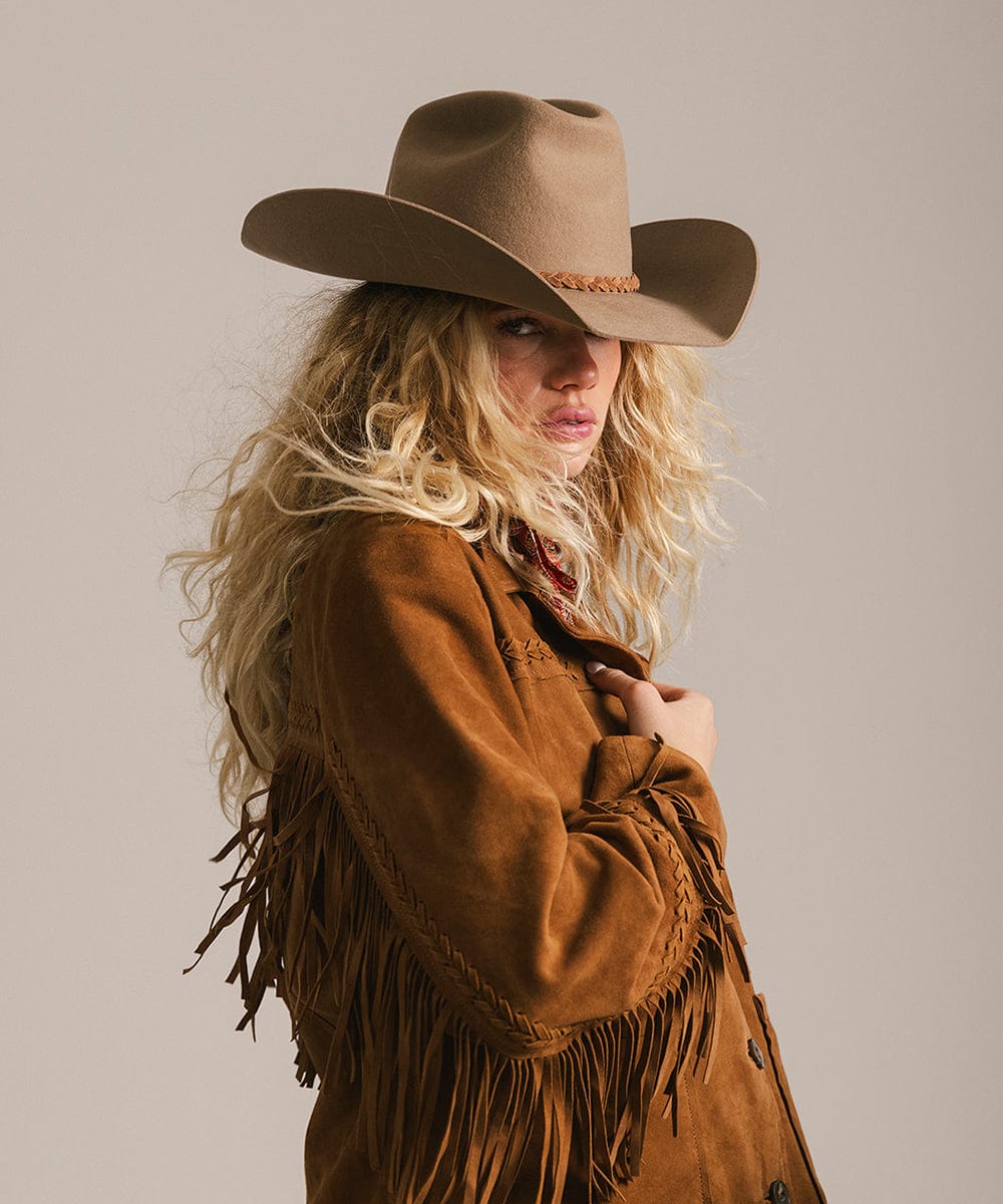 Woman wearing a brown cowboy hat and fringed jacket against a plain background #color_brown