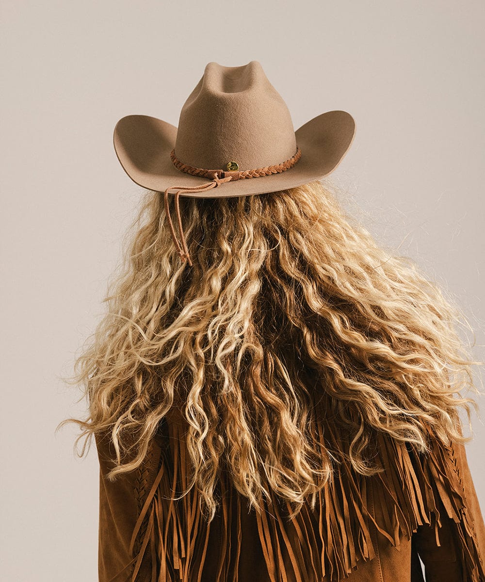 Person wearing a tan cowboy hat and fringed jacket on a plain background #color_brown