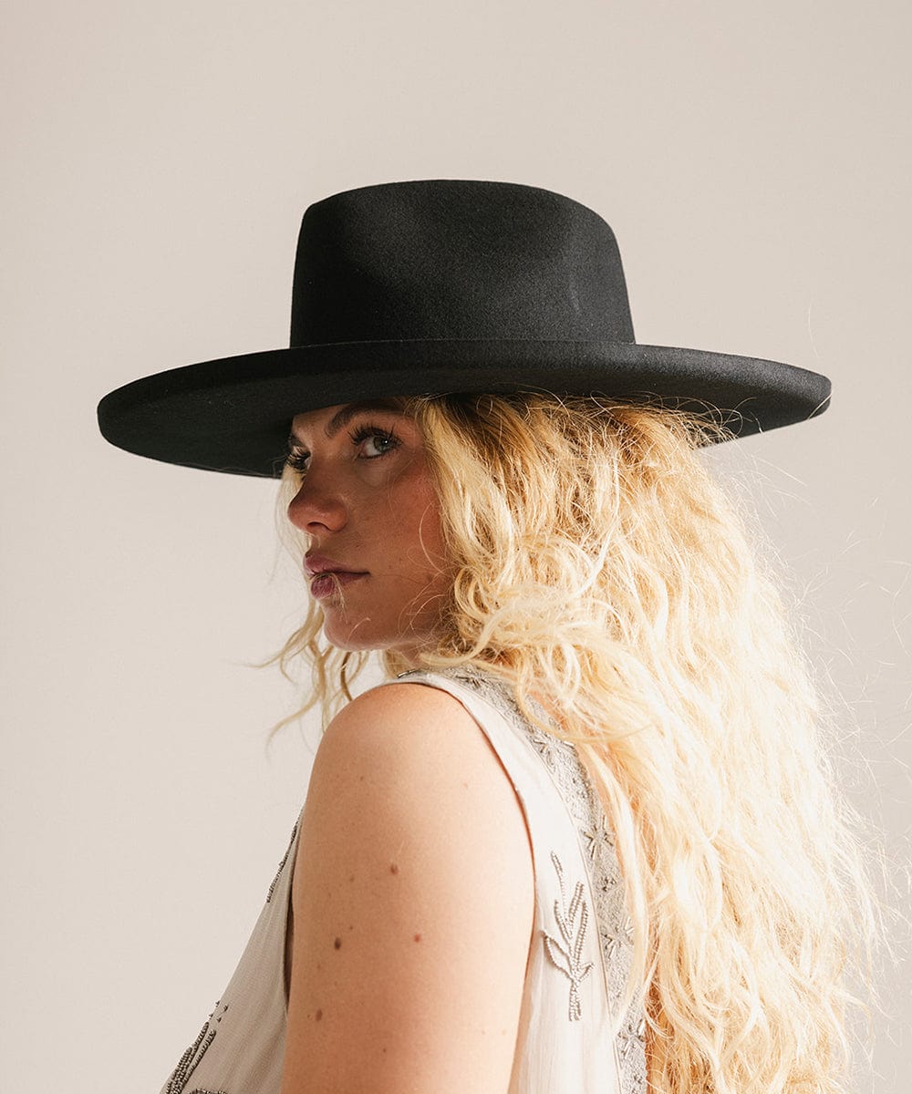 Woman wearing a black hat and a light colored dress, looking sideways against a plain background #color_black