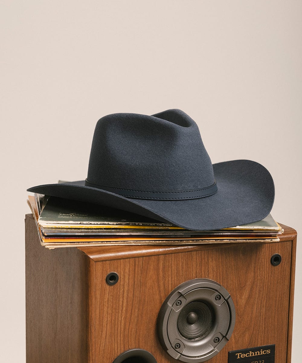 Vintage blue cowboy hat with a hat band on top of a wooden Technics record player against a plain background #color_vintage blue