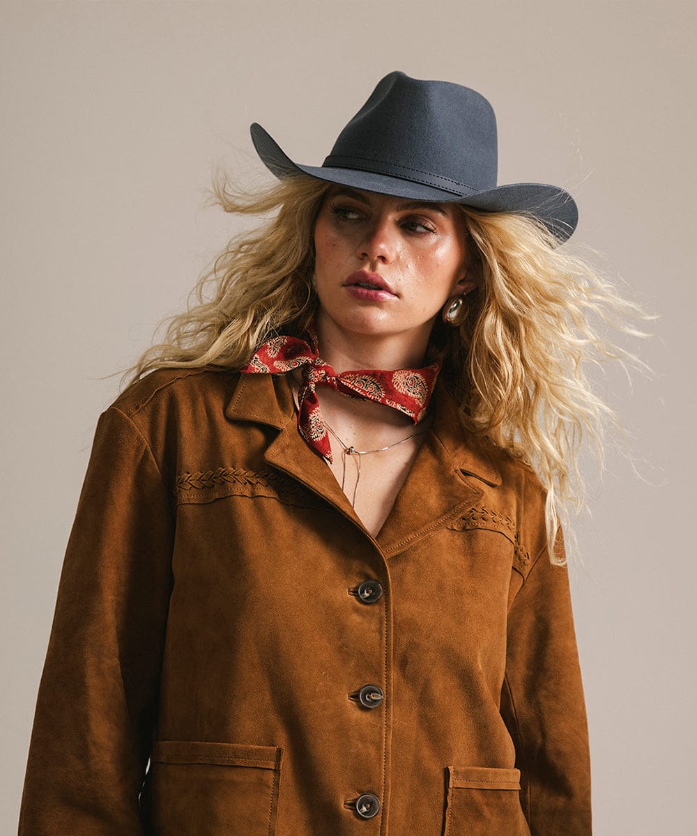 Woman wearing a vintage blue colored cowboy hat with a hat band  and a brown jacket with a scarf against a plain background #color_vintage blue
