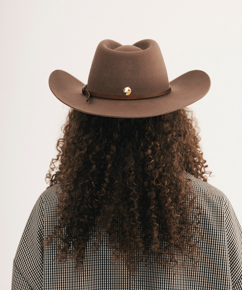 Woman wearing a brown cowboy hat with a brown hat band and a plaid shirt #color_chocolate