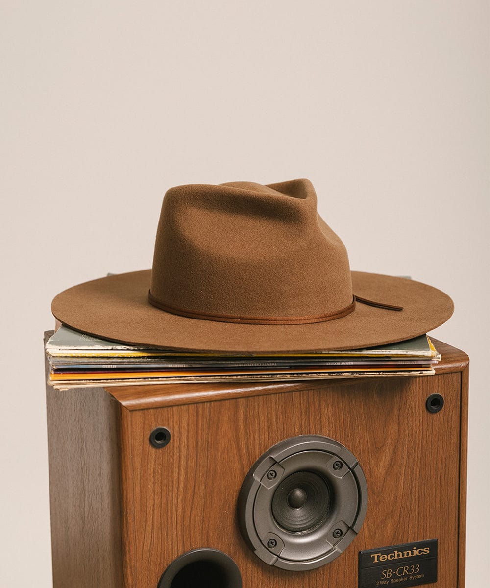 Caramel colored fedora hat with a hat band on top of a Technics record player with records stacked inside, against a plain background #color_caramel