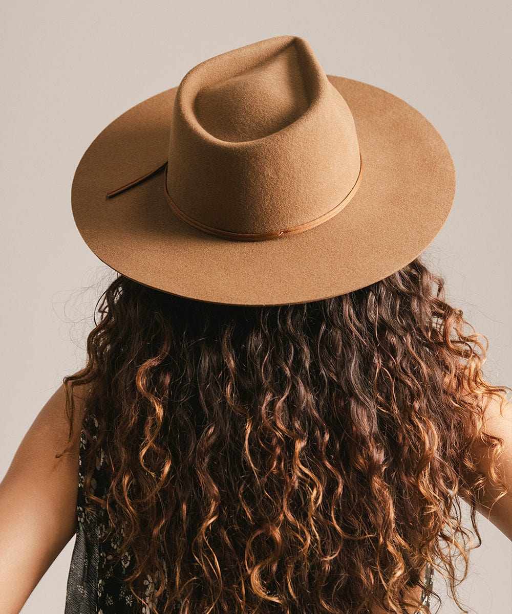 Woman wearing a caramel colored fedora hat with a hat band facing behind against a plain background #color_caramel