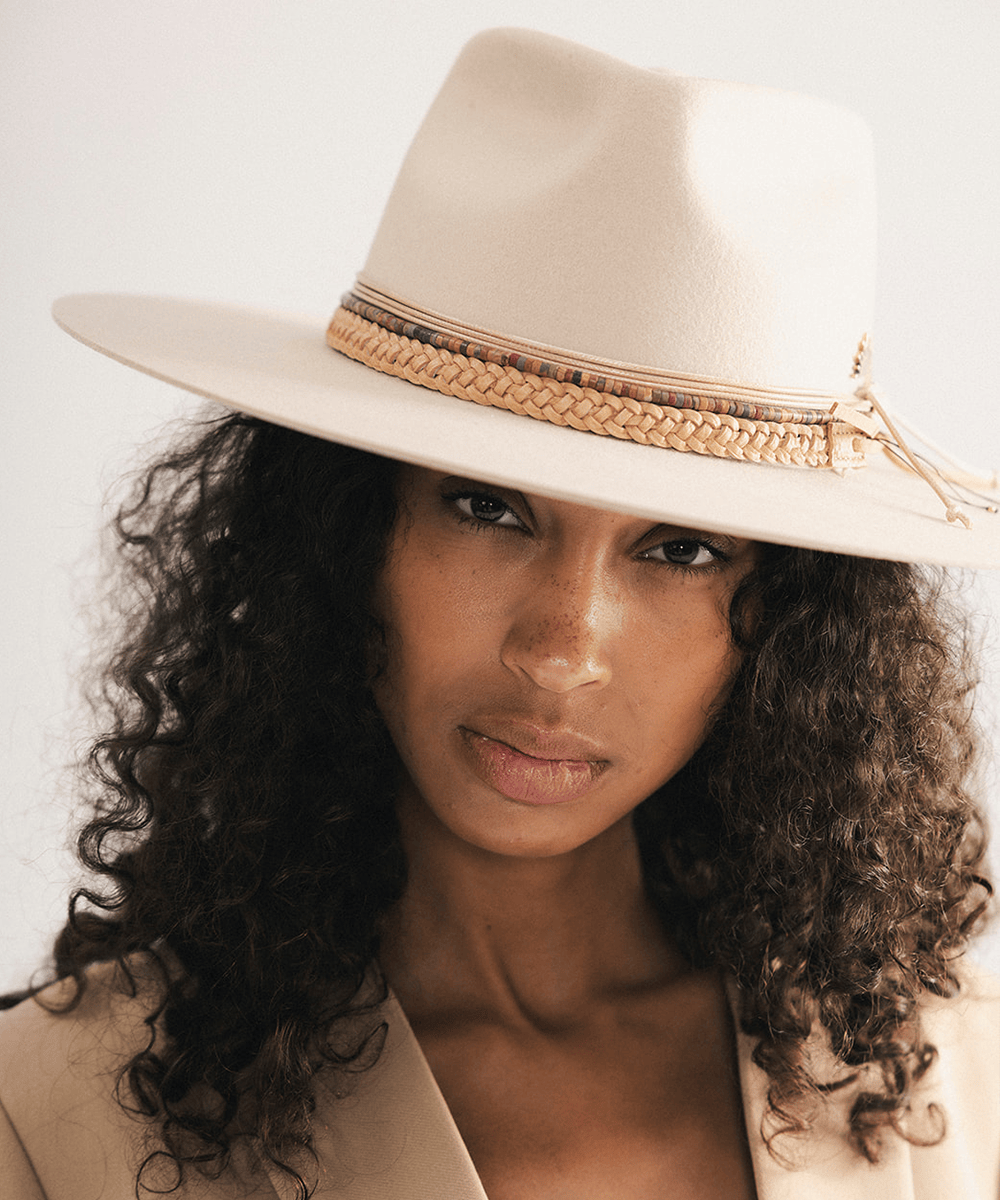 Woman wearing a beige cowboy hat with braided detail against a white background #color_tan