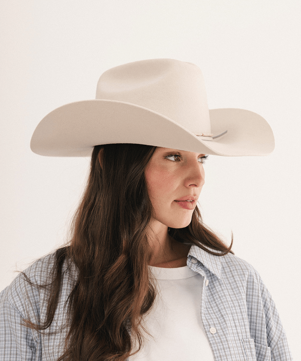A woman wearing a light beige cowboy hat, styled with a blue and white plaid button-down shirt over a white t-shirt, photographed against a clean white background #color_off white