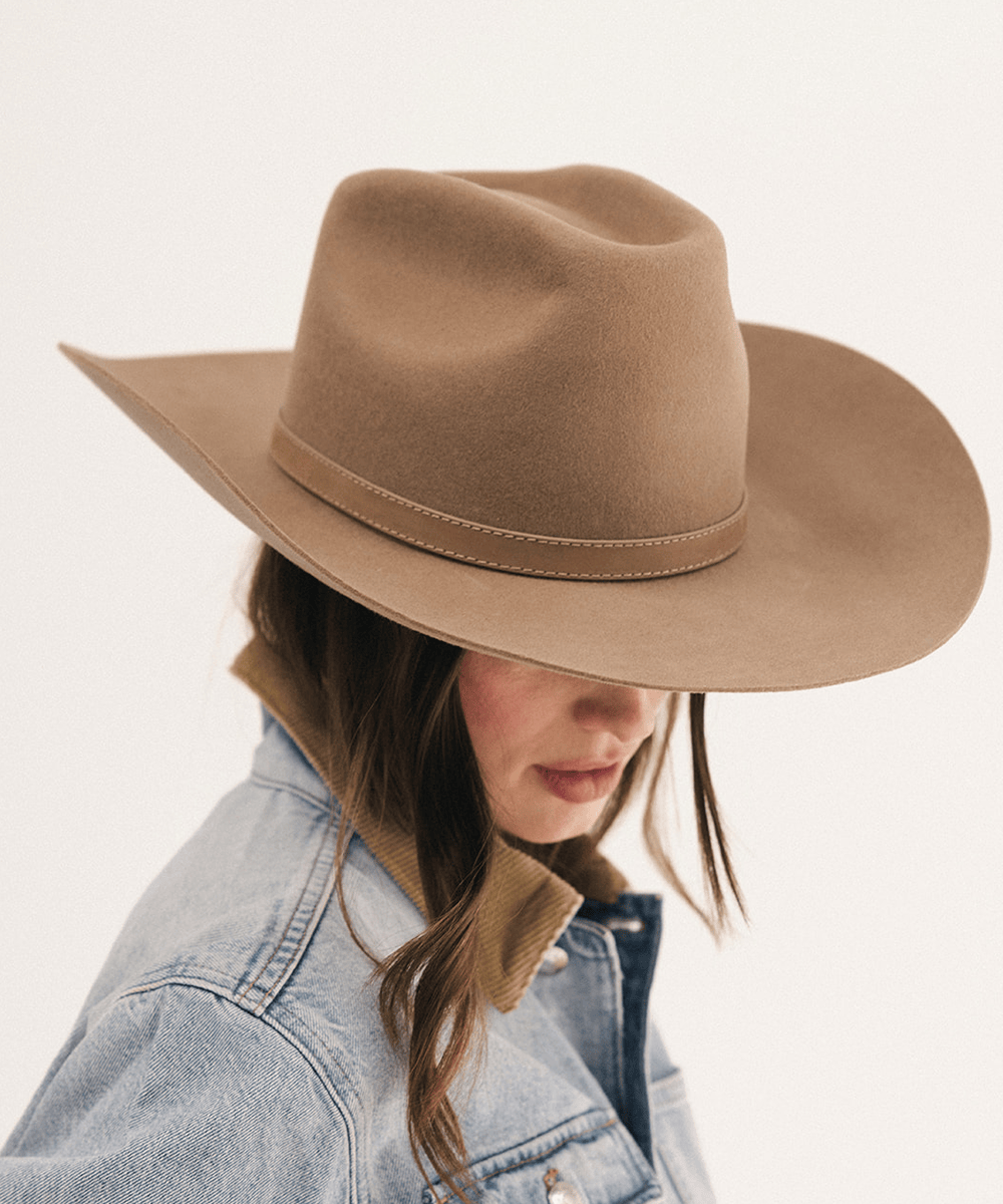 A woman wearing a wide-brimmed tan cowboy hat and a light blue denim jacket, shown in profile against a plain white background #color_brown