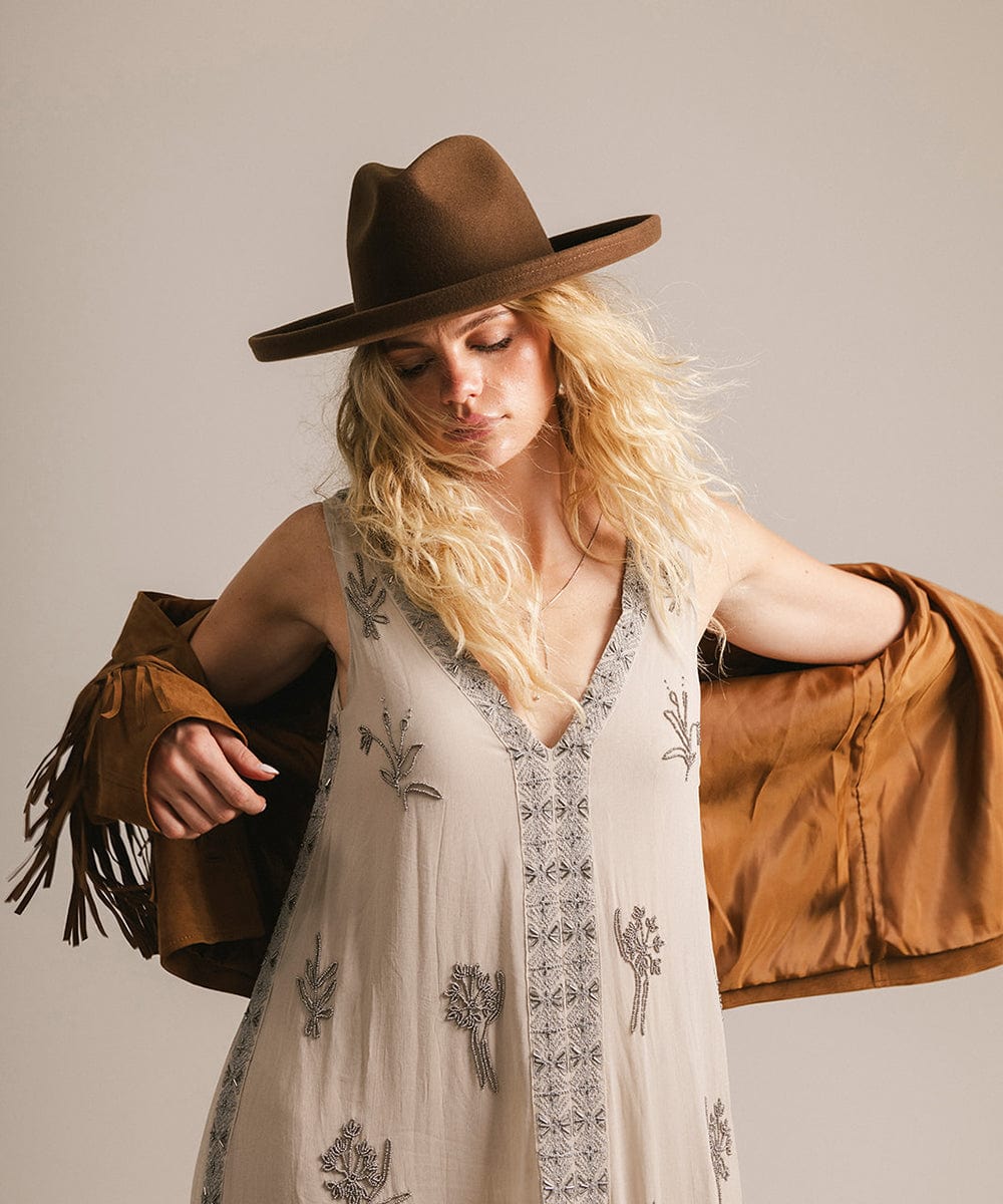 Woman wearing a chocolate colored pencil brim felt fedora hat and a dress with a brown jacket against a neutral background #color_chocolate