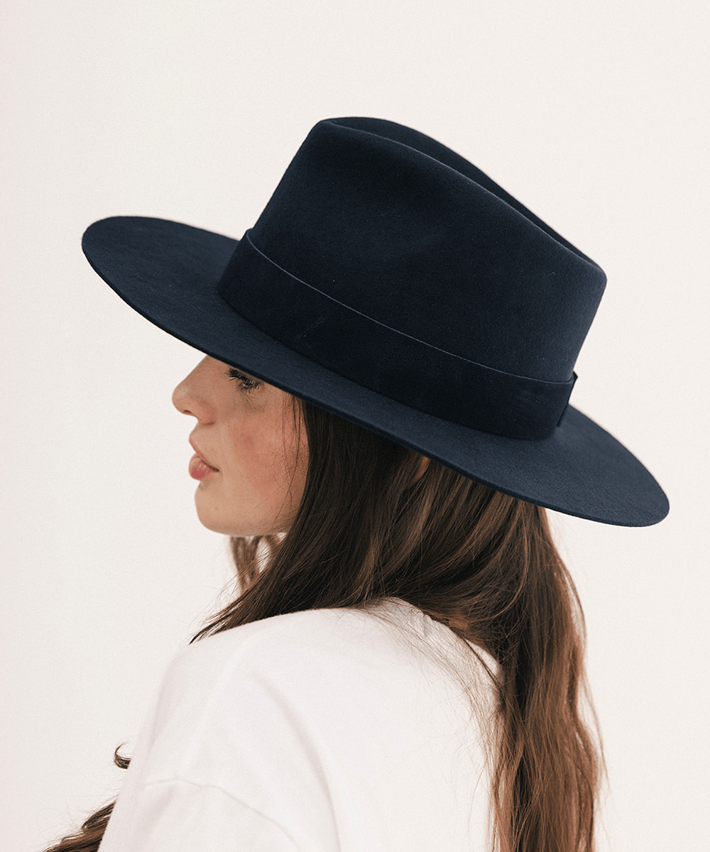 A woman in profile wearing a wide-brimmed black felt hat with a matching band, photographed against a clean off-white background #color_navy