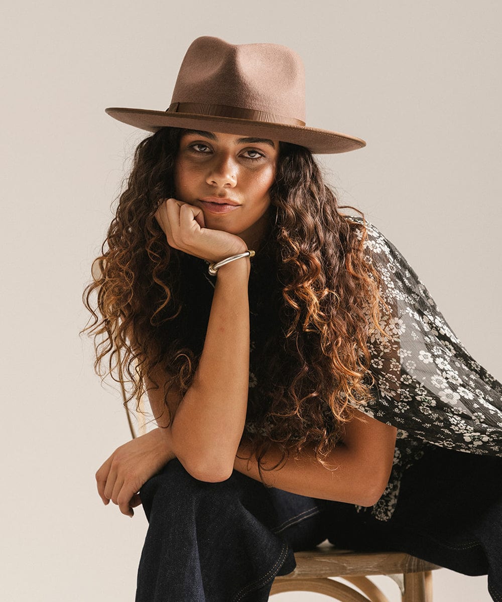 Woman wearing a chocolate colored hat, a floral top and dark blue jeans, sitting on a chair against a plain background #color_chocolate