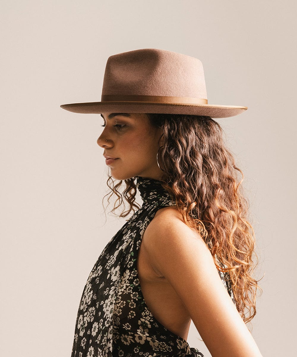 Woman wearing a chocolate colored hat and a floral top, facing sideways against a plain background #color_chocolate