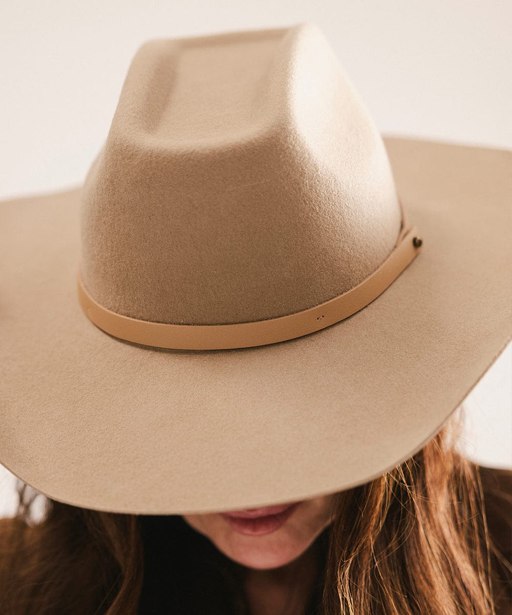Woman wearing a tan cowboy hat with an upturned brim and an attached leather band against a plain background #color_tan