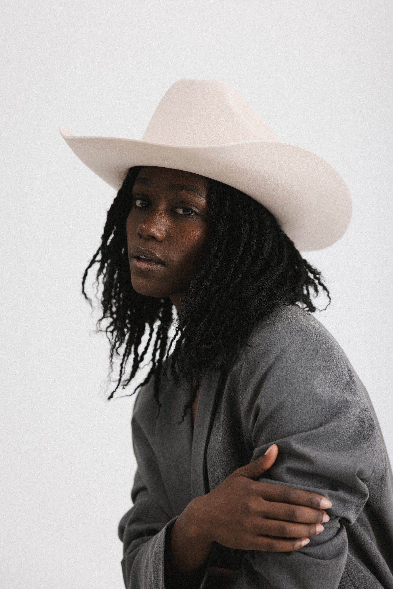 Woman wearing a cream cowboy hat and grey blazer, posing against a white background #color_cream