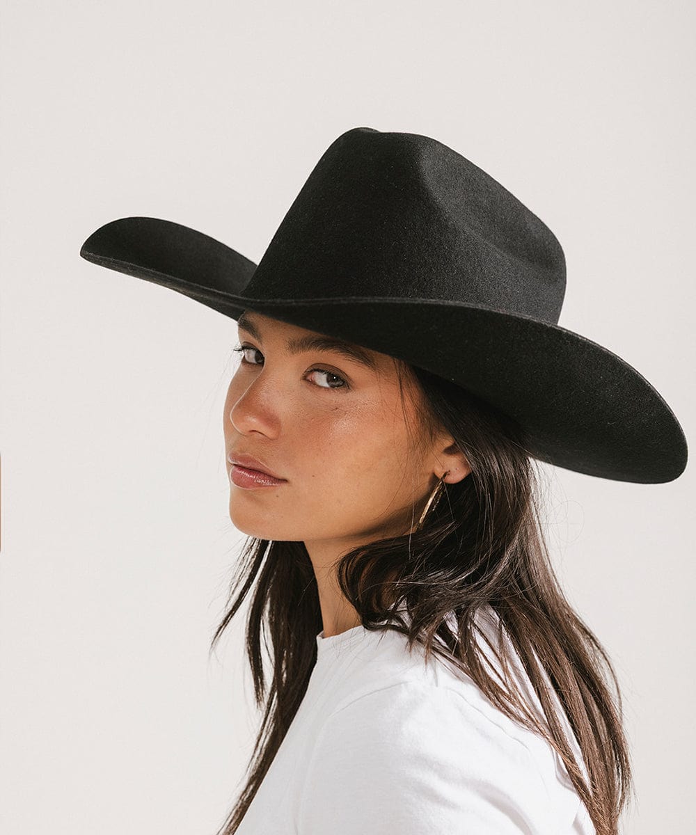 Woman wearing a black cowboy hat and a white t-shirt, posing sideways against a plain background #color_black