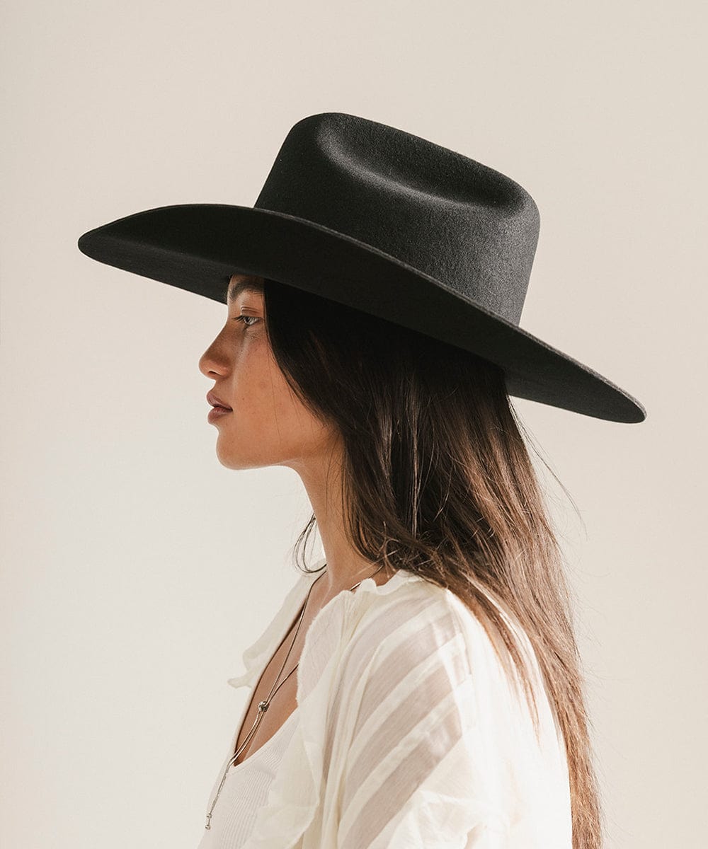 Woman wearing a black cowboy hat and a white shirt, facing sideways against a plain background #color_black