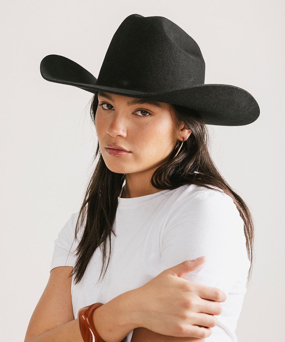 Woman wearing a black cowboy hat and a white t-shirt, posing against a plain background #color_black