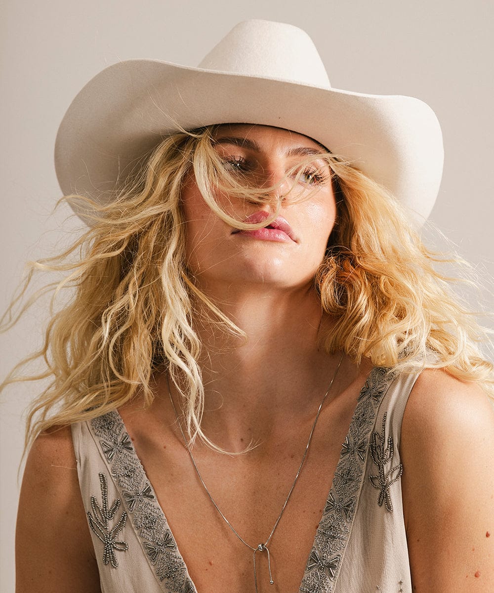 Woman wearing an off white cowboy hat against a plain background #color_off white