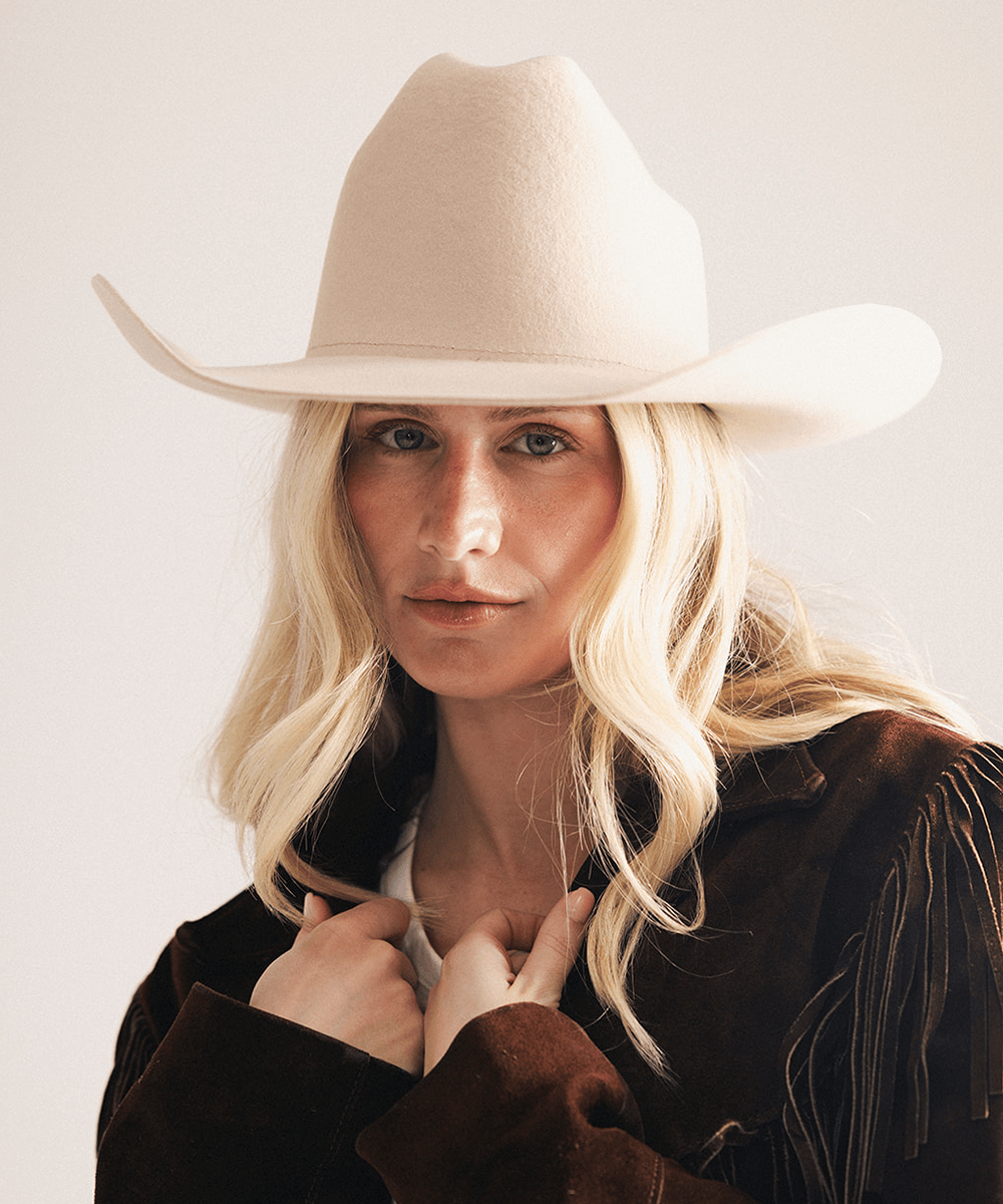 Woman wearing a beige cowboy hat and brown jacket on a light background #color_cream