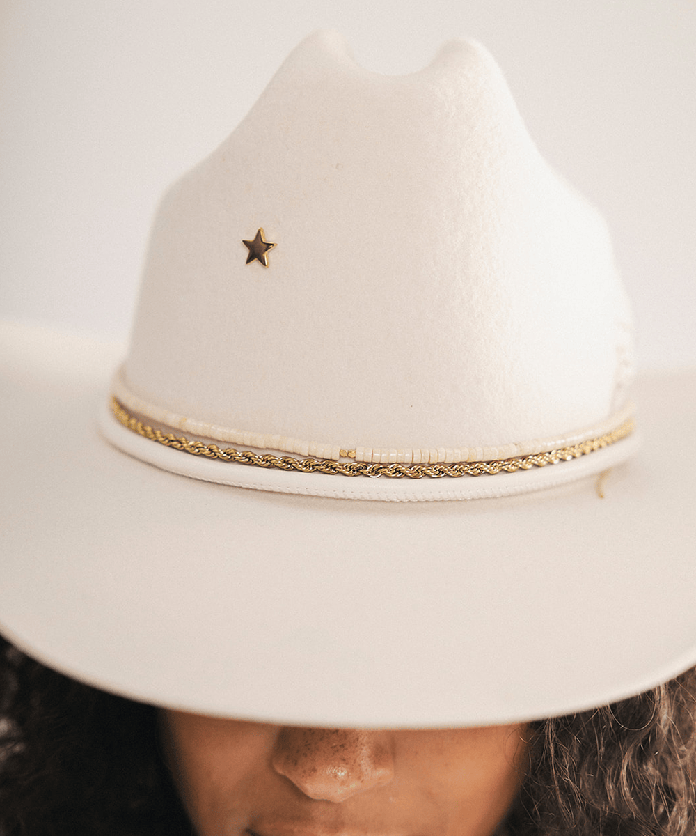 Woman wearing a white cowboy hat with a decorative band and a star pin on a plain background #color_off white