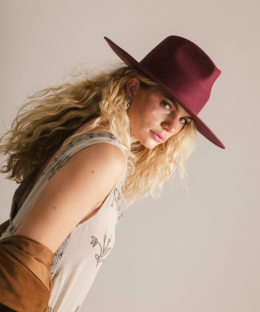 Woman wearing a merlot fedora hat and a dress against a plain background #color_merlot