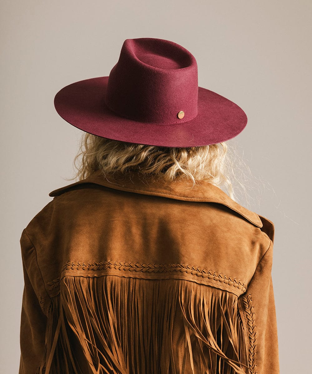 Person wearing a brown fringed jacket and merlot fedora hat, facing behind against a plain background #color_merlot
